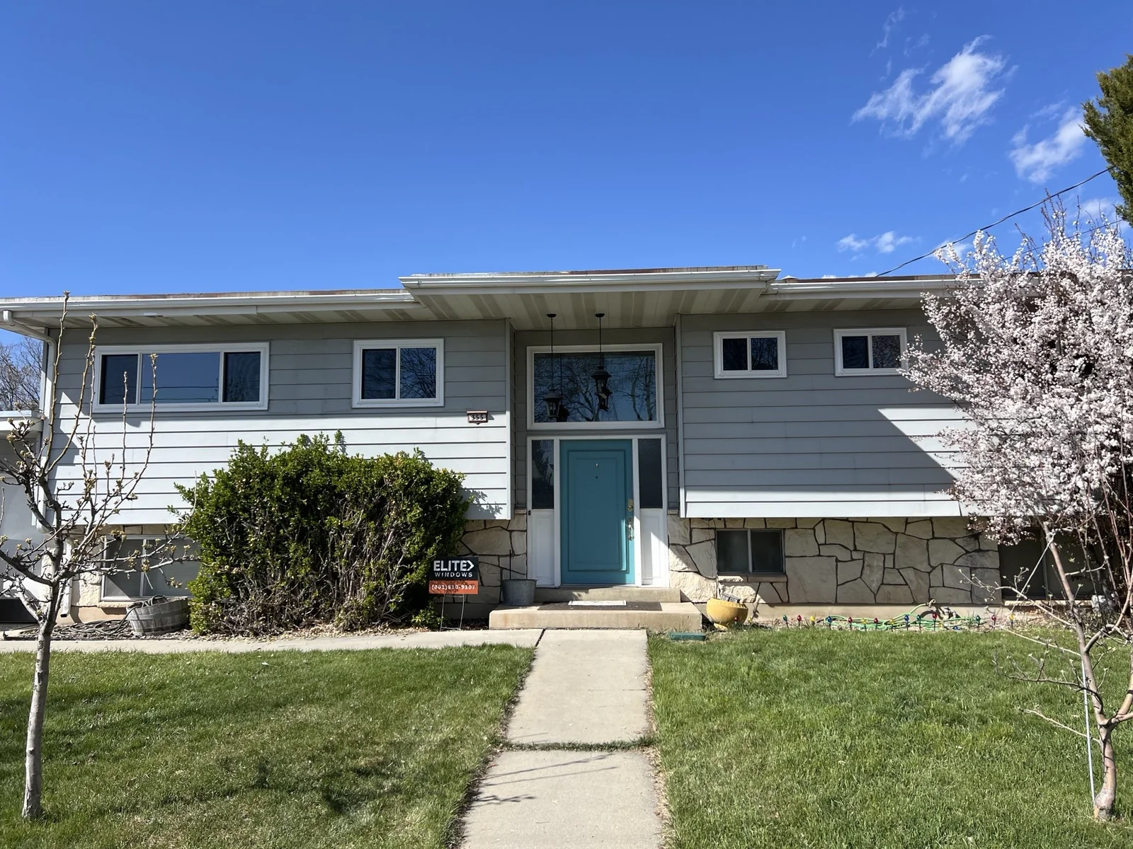 White replacement windows on a siding and stone home with a blue door
